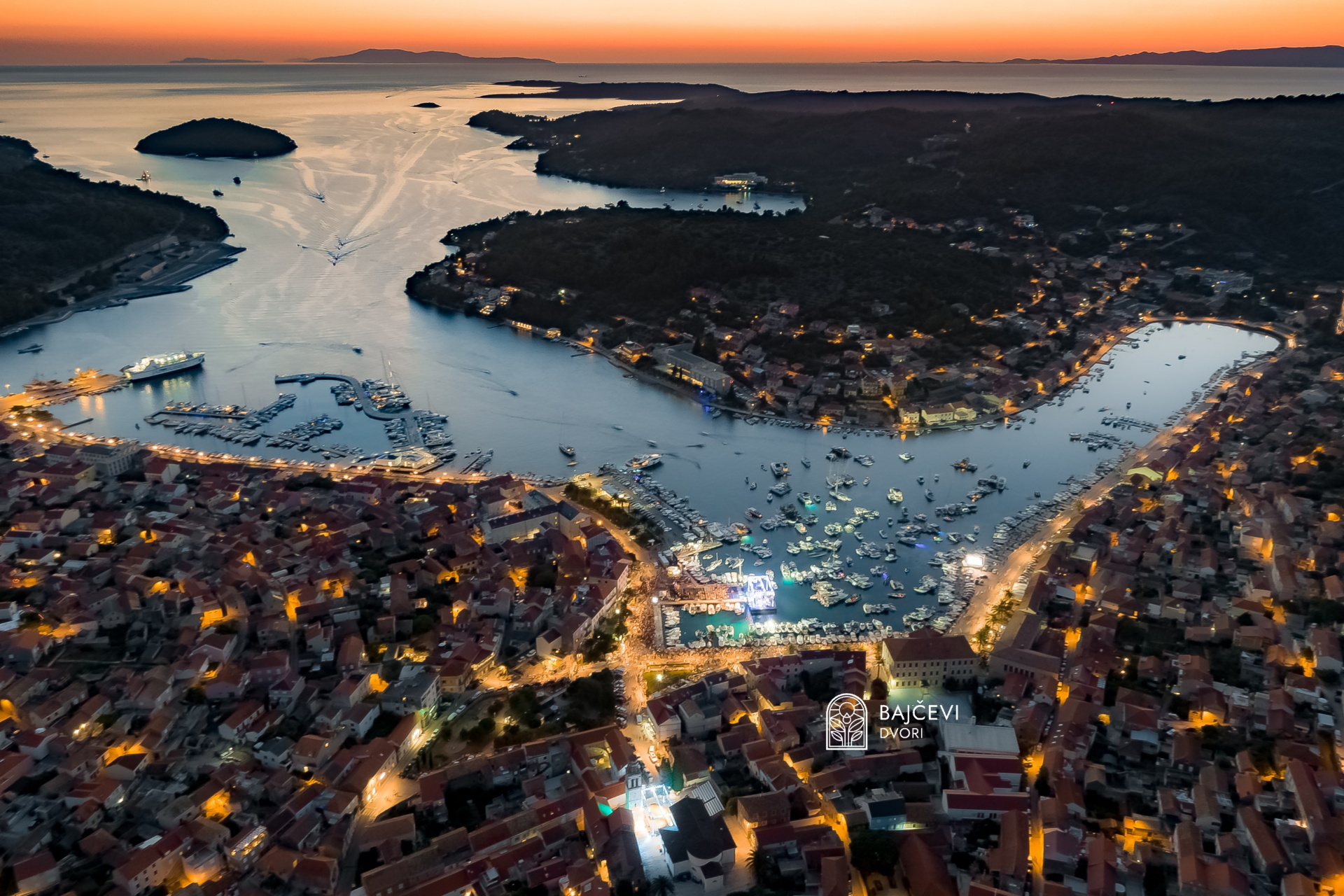 Vela Luka aerial view at dusk with Bajčevi Dvori emblem